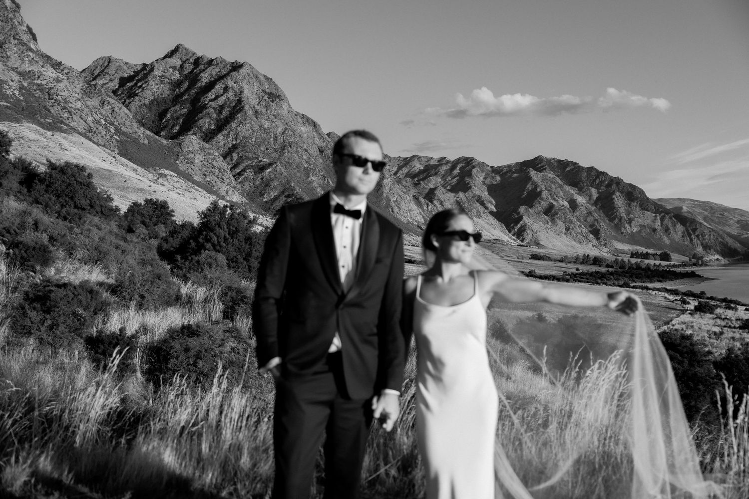 Couple in formal attire posing against dramatic mountain landscape.