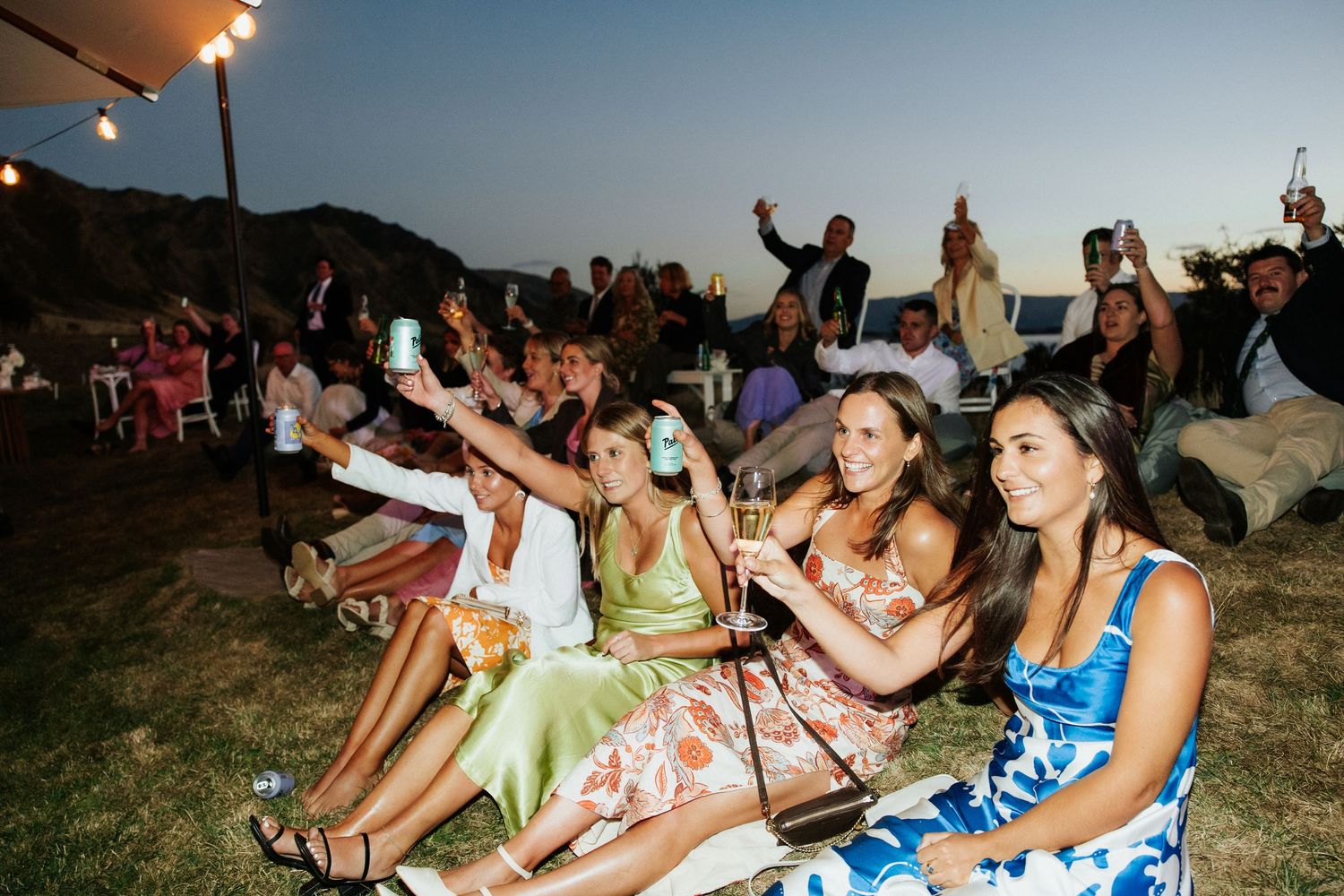 Wedding guests enjoying outdoor reception celebration against mountain backdrop.