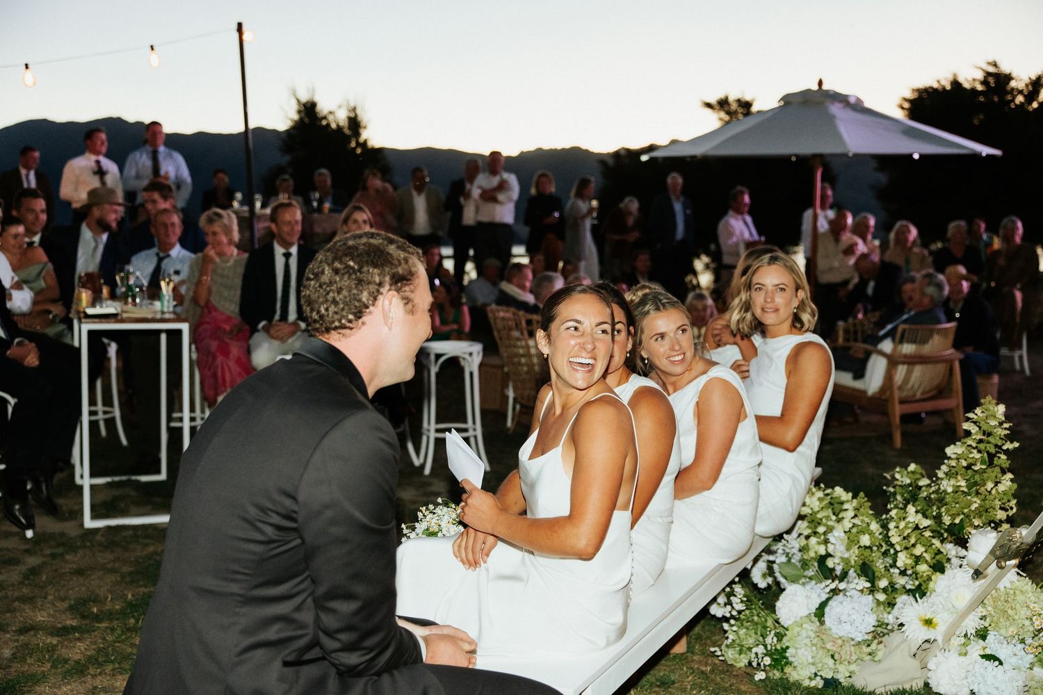 Wedding party members share laughter during an outdoor reception celebration.