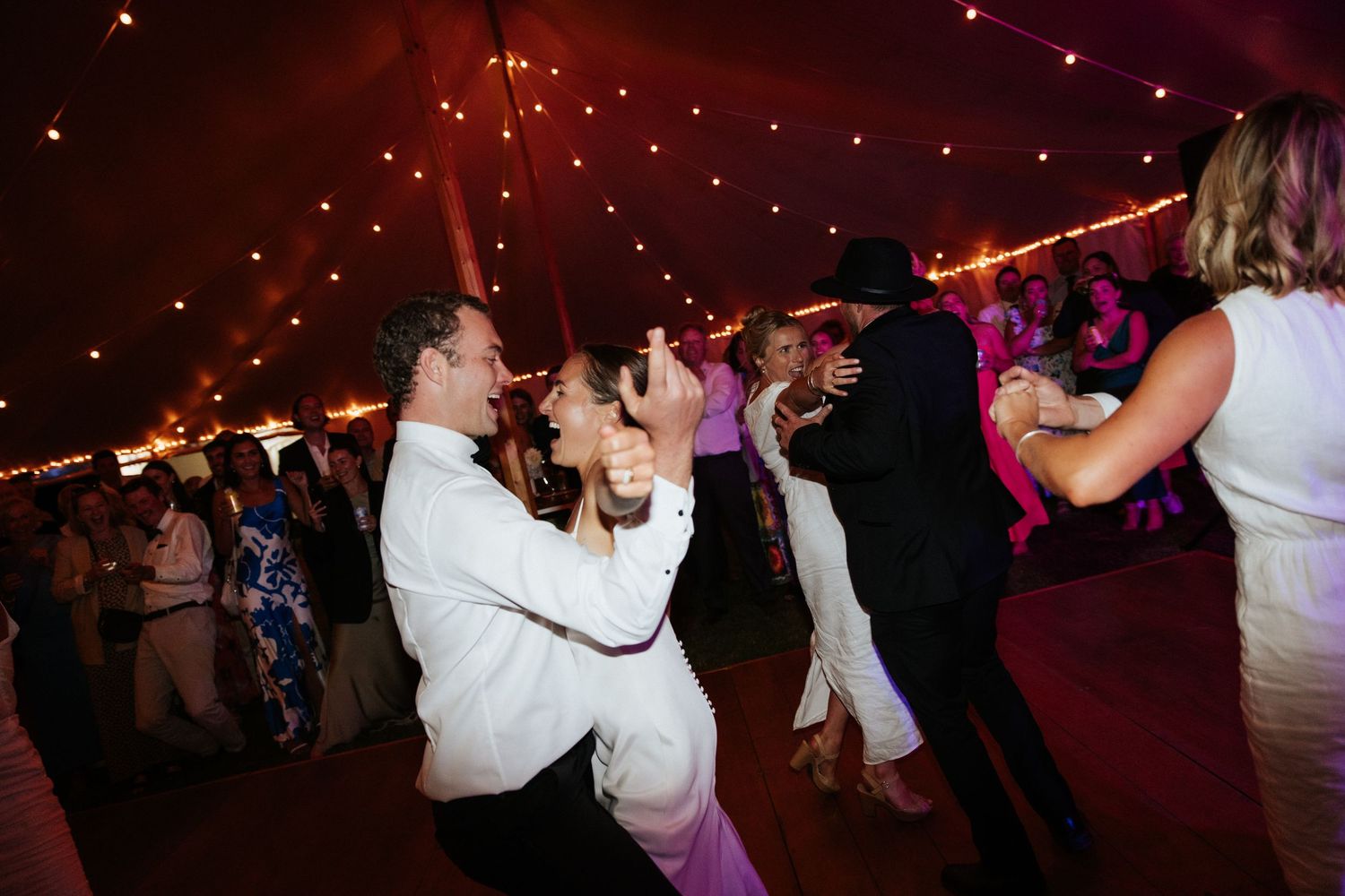 Wedding reception dance party with couples dancing under string lights.