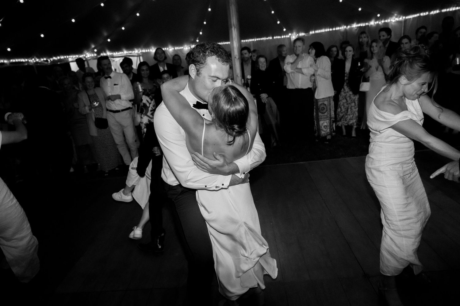 Dancing couples at evening wedding reception under string lights in black and white photography.