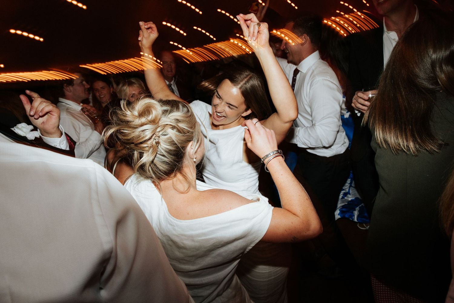Wedding reception dance party with enthusiastic guests celebrating on dance floor.