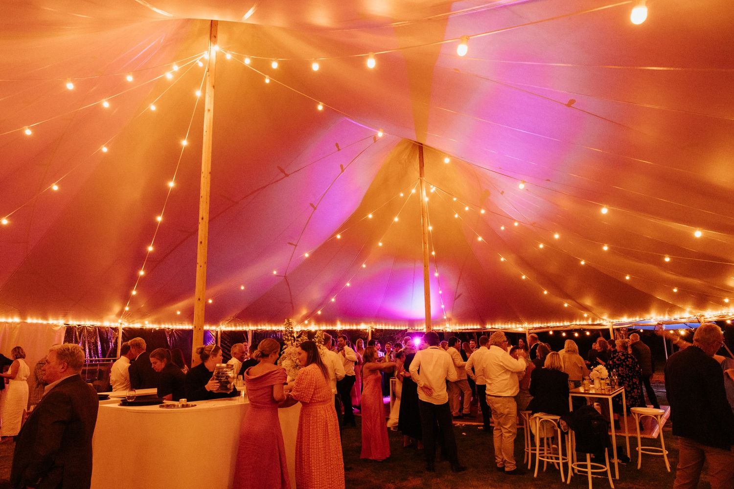 Wedding reception under glowing tent with warm lighting creating romantic orange and pink ambiance.