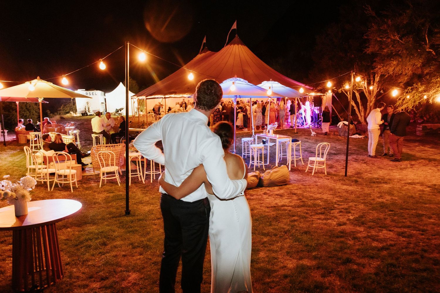 Reception venue at night with illuminated tent and couple overlooking decorated outdoor space.