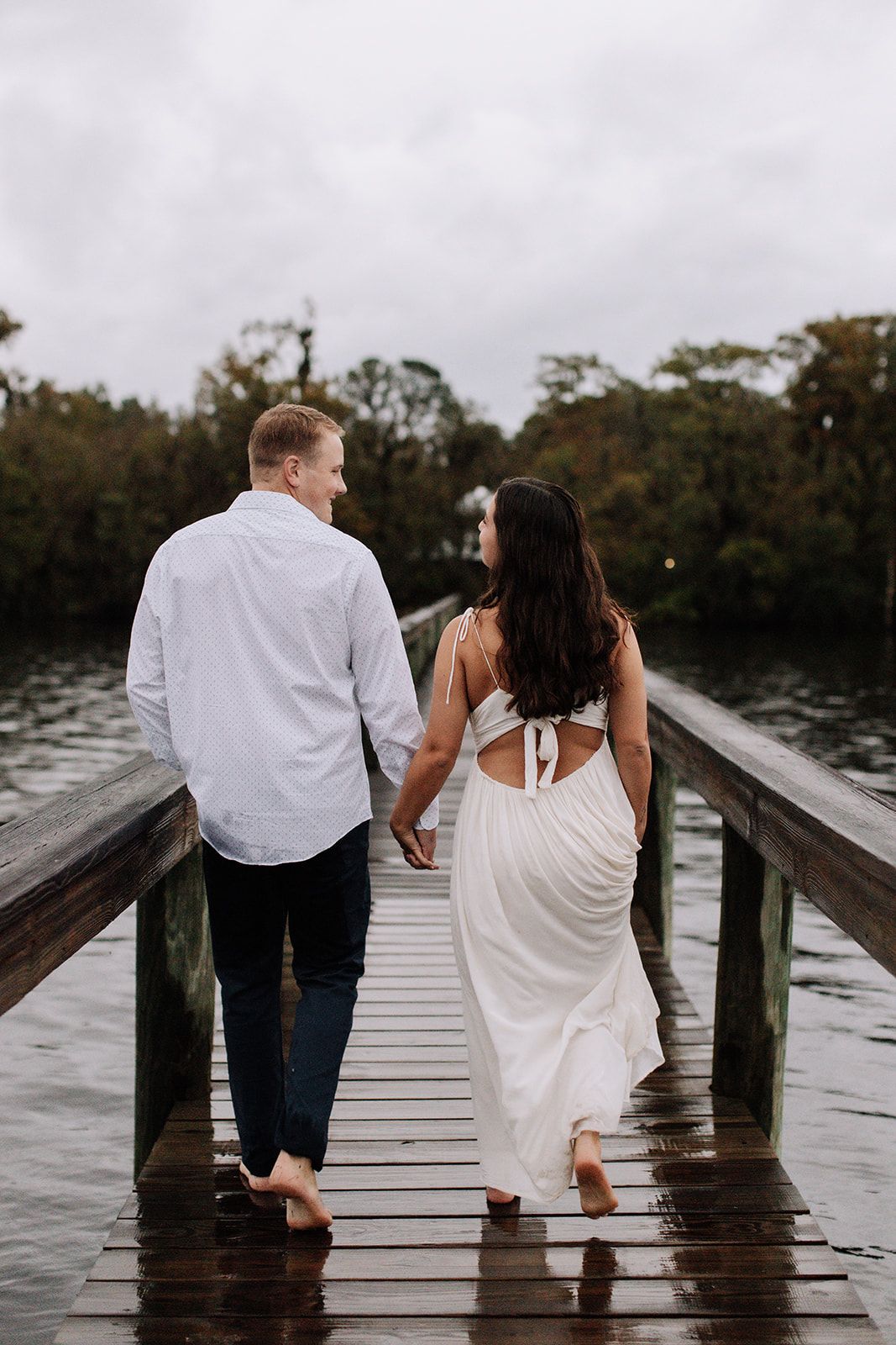 Couple dancing together on a wooden dock by the lake in black and white, with the woman wearing a flowing white dress.