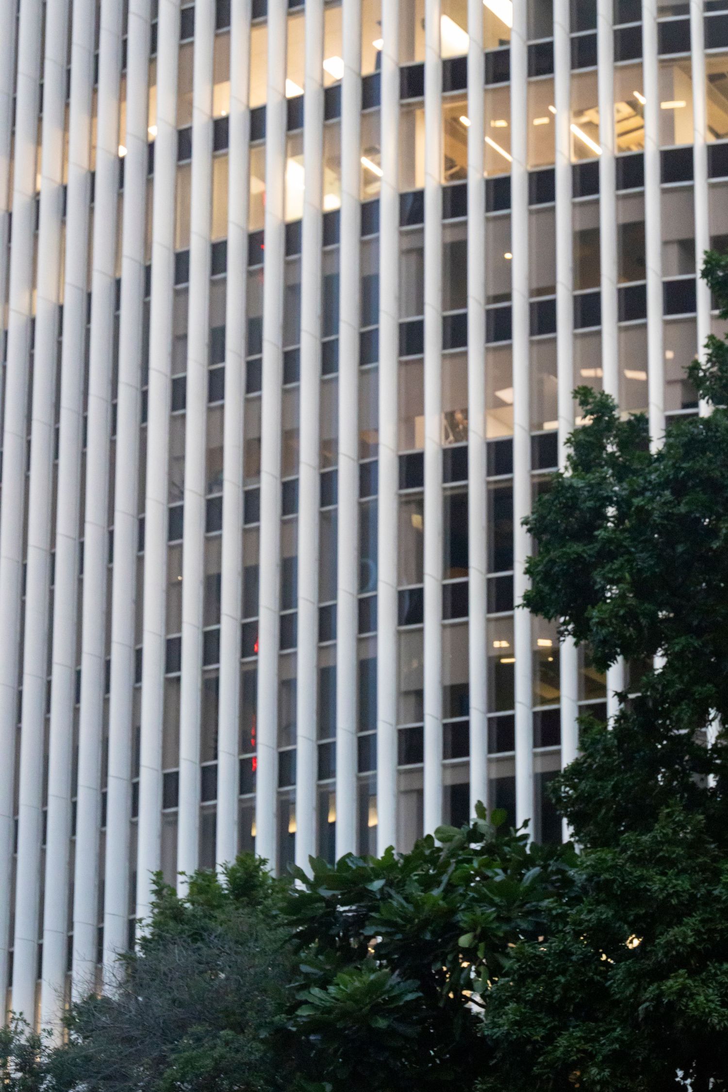 Tall office building with repeating vertical fins and golden light peeking through.