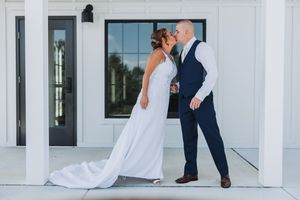 A couple shares a tender moment on a white porch during their wedding day, with the bride in a flowing white dress.