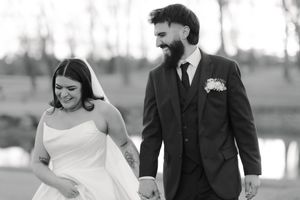 Black and white portrait of happy newlyweds in formal wedding attire sharing a candid moment outdoors.