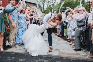 Newly married couple performs romantic dip during celebration ceremony while guests cheer and smile along the sides.