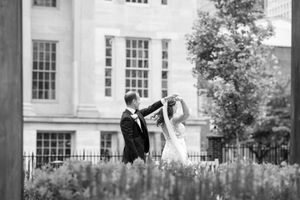 A romantic couple dancing together in a garden with a grand white building in the background, captured in black and white.