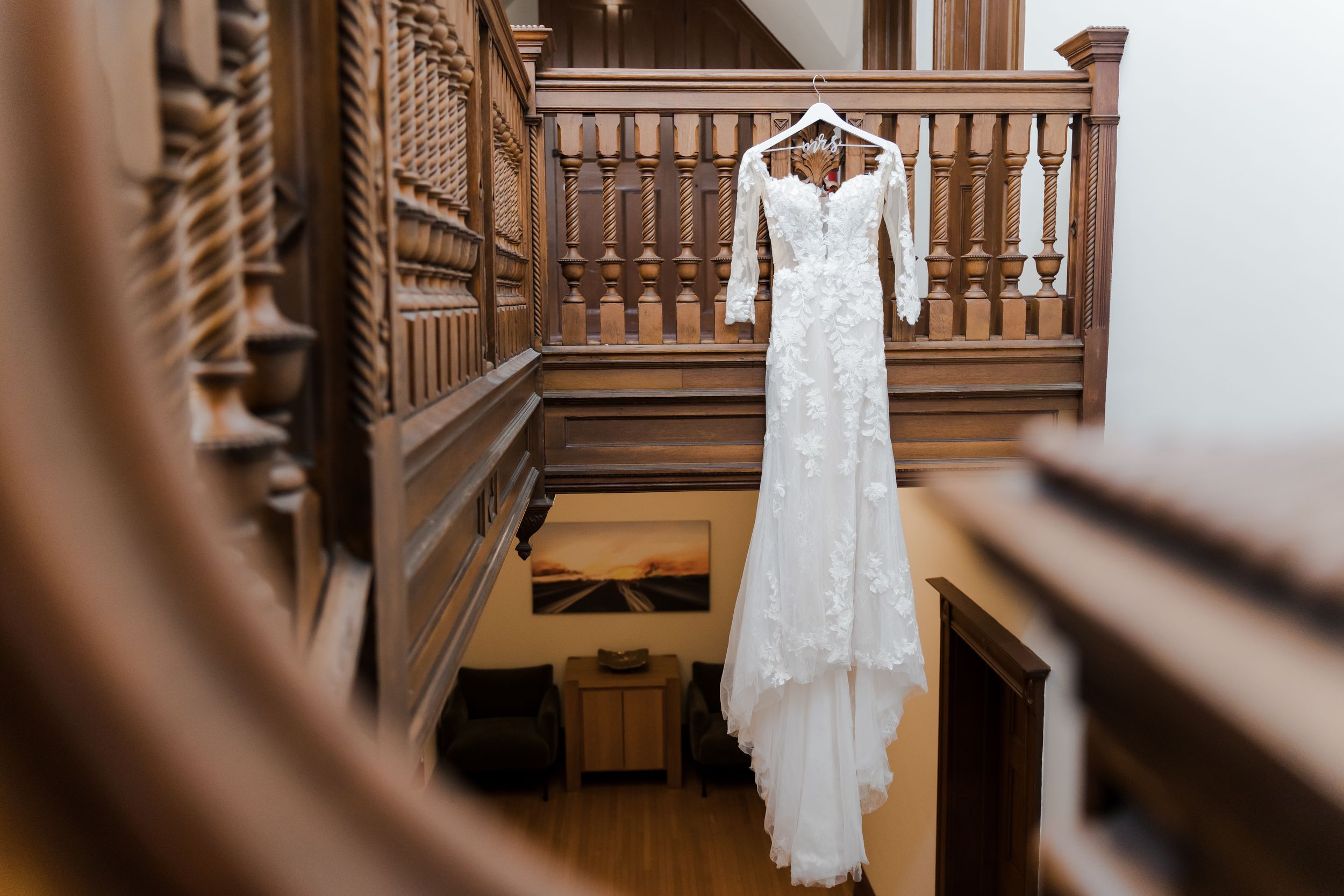 White lace wedding dress hanging on wooden staircase banister in elegant venue.