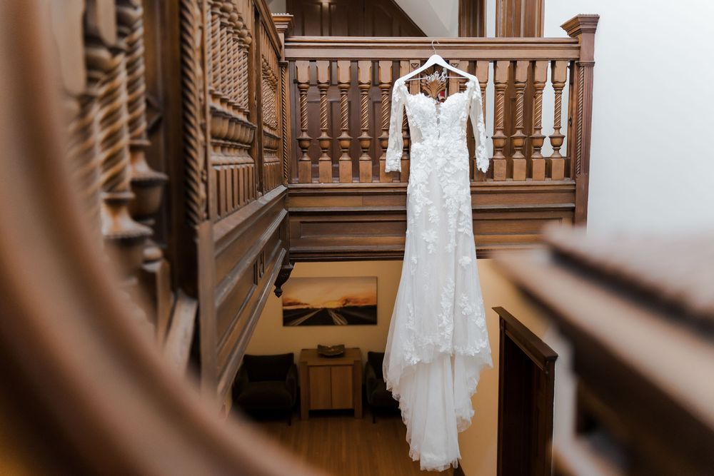 White lace wedding dress hanging on wooden staircase banister in elegant venue.