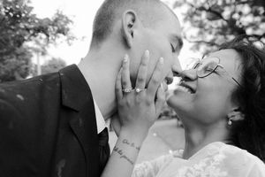 Black and white wedding photo of couple almost kissing, bride wearing ring and lace dress with tattoo visible.