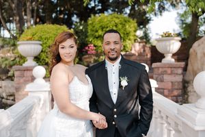 A happy couple poses together on stone steps surrounded by decorative urns and greenery at their wedding ceremony.
