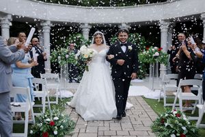 Wedding ceremony with confetti falling at an outdoor garden venue featuring white gazebo and floral decorations along the aisle.