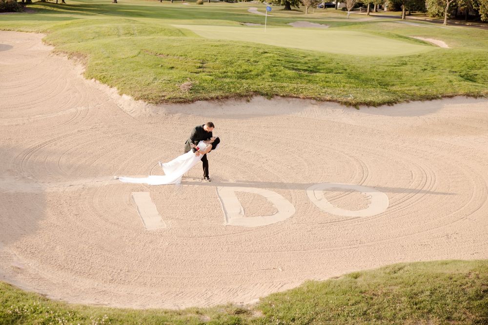 Golfer takes a swing from a sand bunker on a scenic golf course surrounded by green grass and trees.