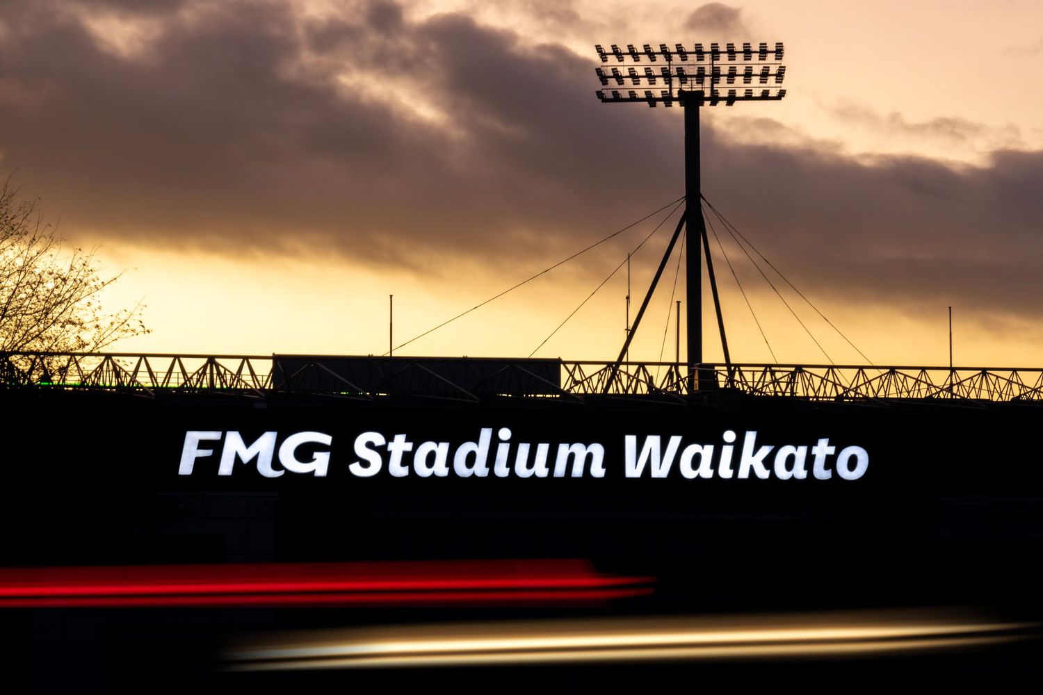 FMG Stadium Waikato sign under glowing floodlights at sunset.