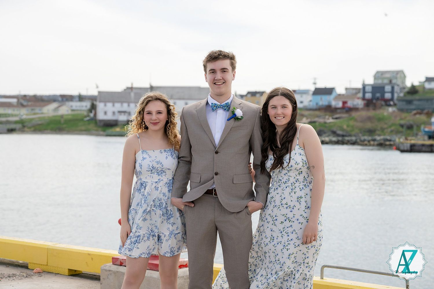 A group poses for photos on a dock by the water, with people wearing gray suits and floral dresses.