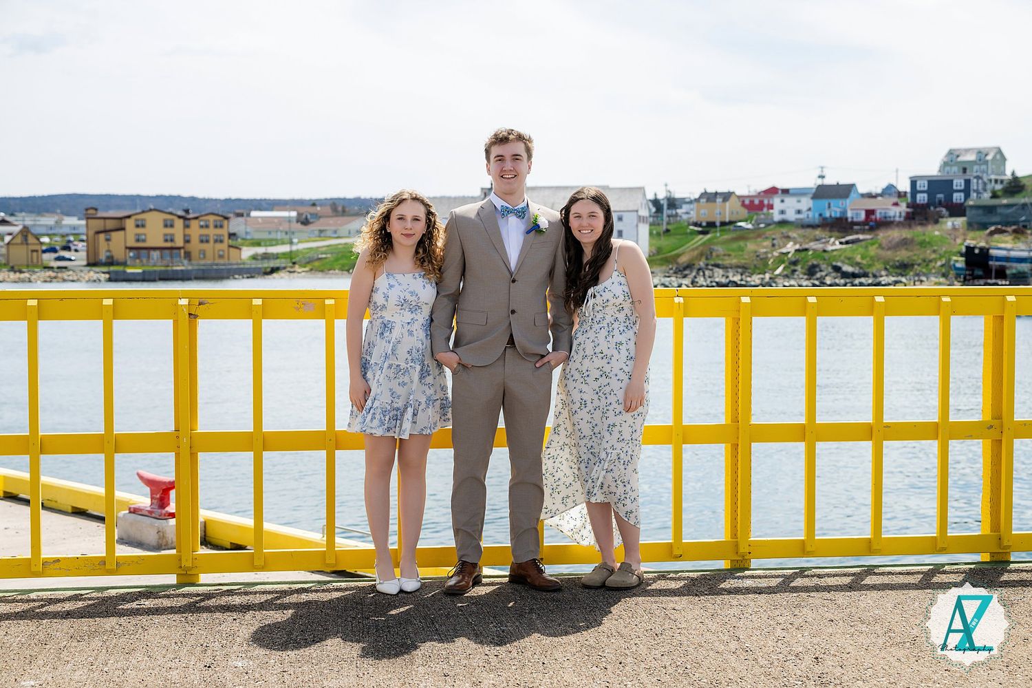 Three people stand together on a yellow bridge railing overlooking a waterfront view on a sunny day.