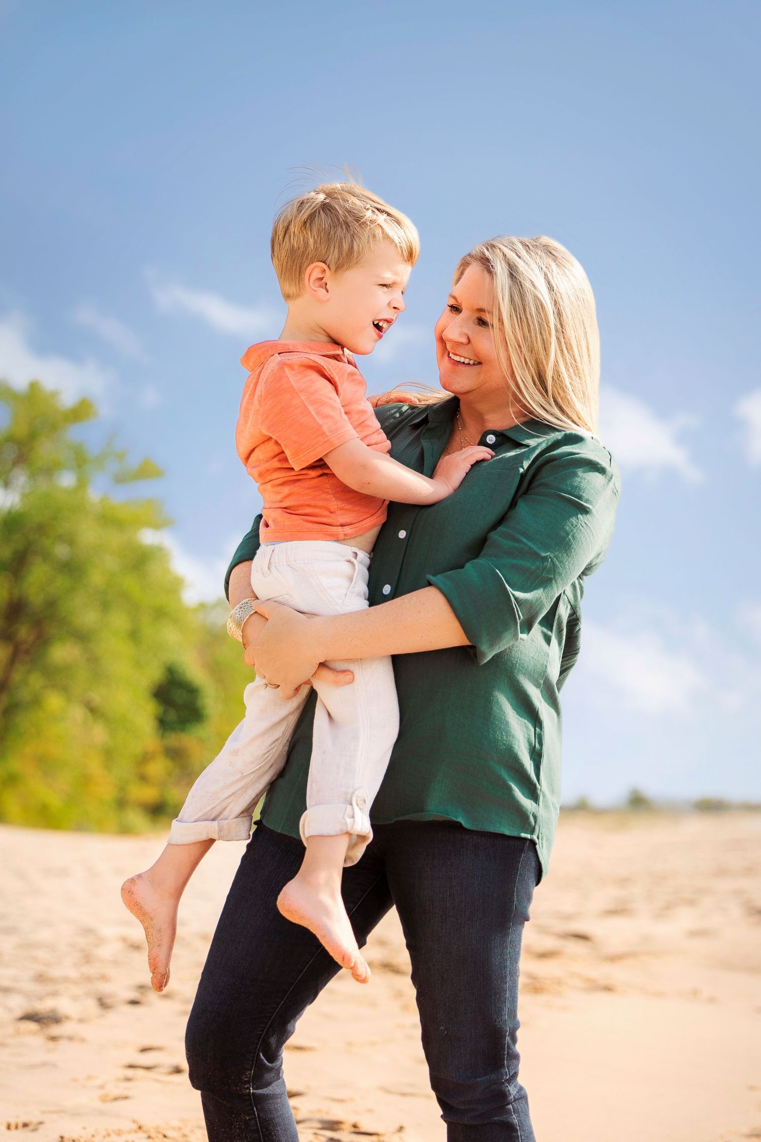 Laughing moment between mom and child as they twirl barefoot in the sand near the shoreline.