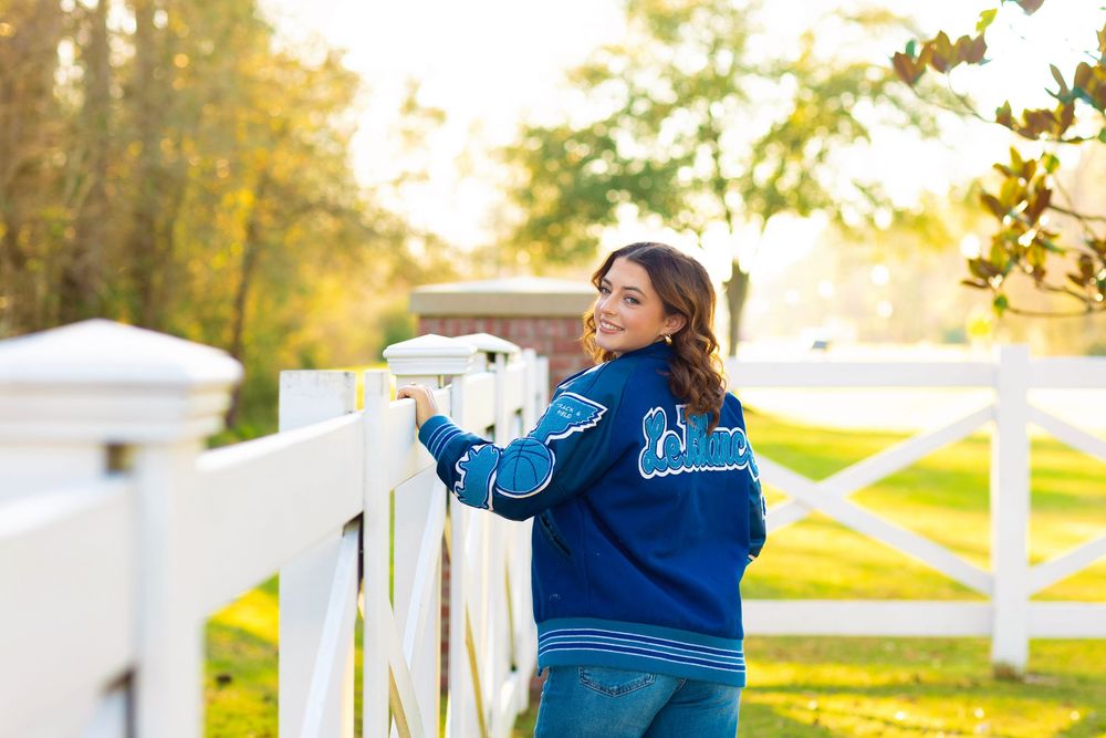 Three people in blue matching outfits walk along a white picket fence during golden hour sunset.