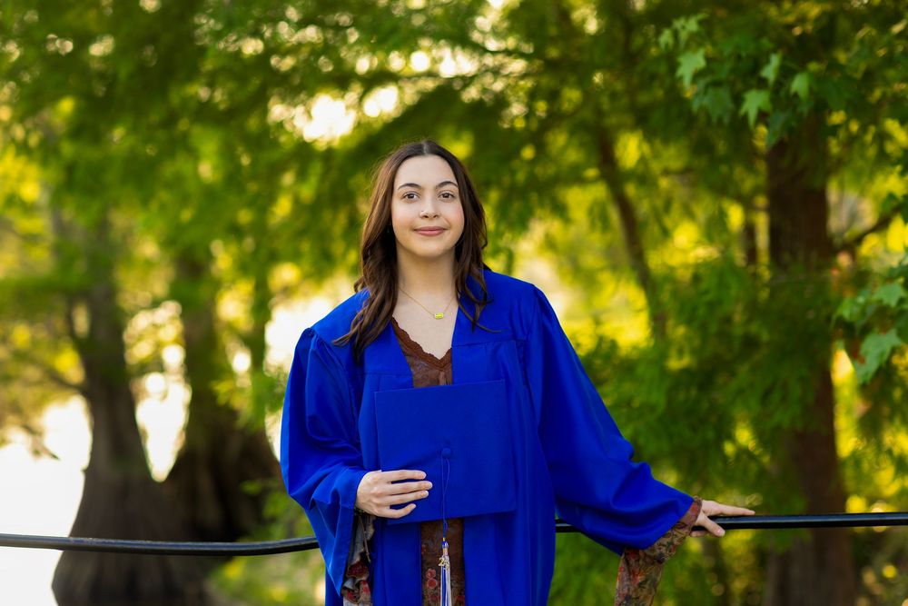 Figure wearing bright blue sweater relaxes against railing in sunlit green park setting.