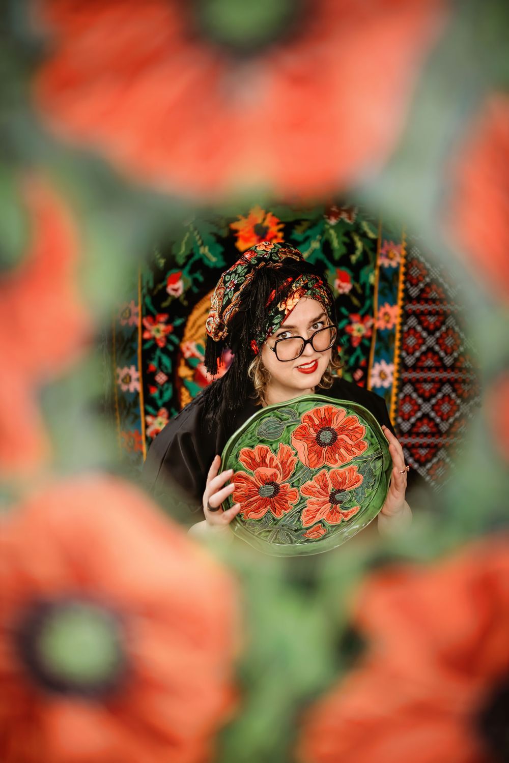 Decorative plate with red poppies held against a floral patterned background with soft bokeh effect creating dreamy atmosphere.