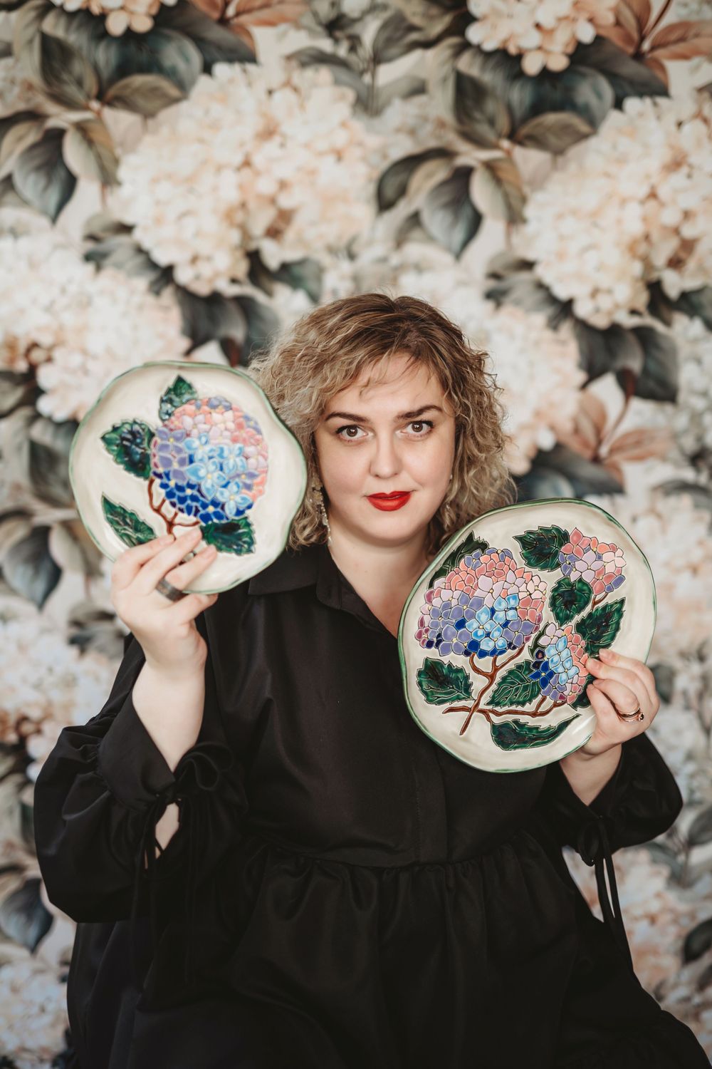 Artist displays handmade embroidered hoops featuring delicate hydrangea designs against a floral backdrop.