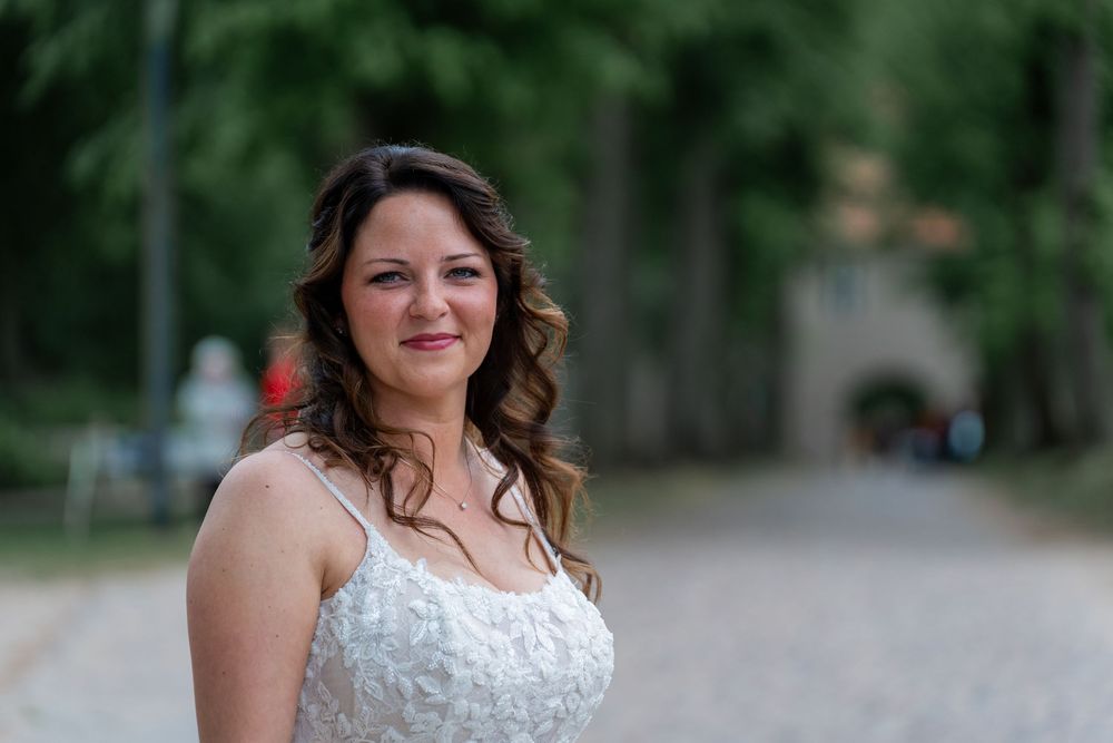 Braut im weißen Kleid lächelt in die Kamera, Bäume im Hintergrund, Schloss Mirow