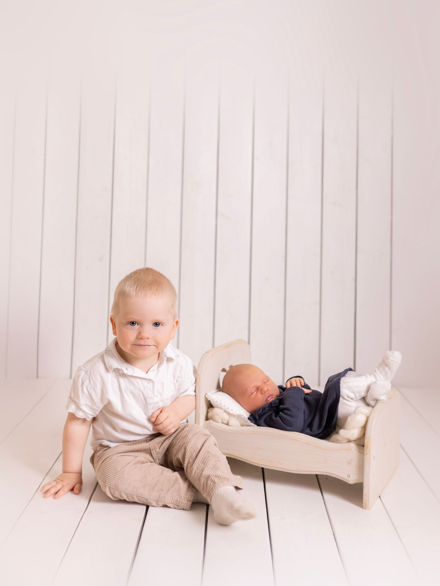 Baby wearing pink headband sits in white wooden barrel prop with peach roses for newborn photography session.
