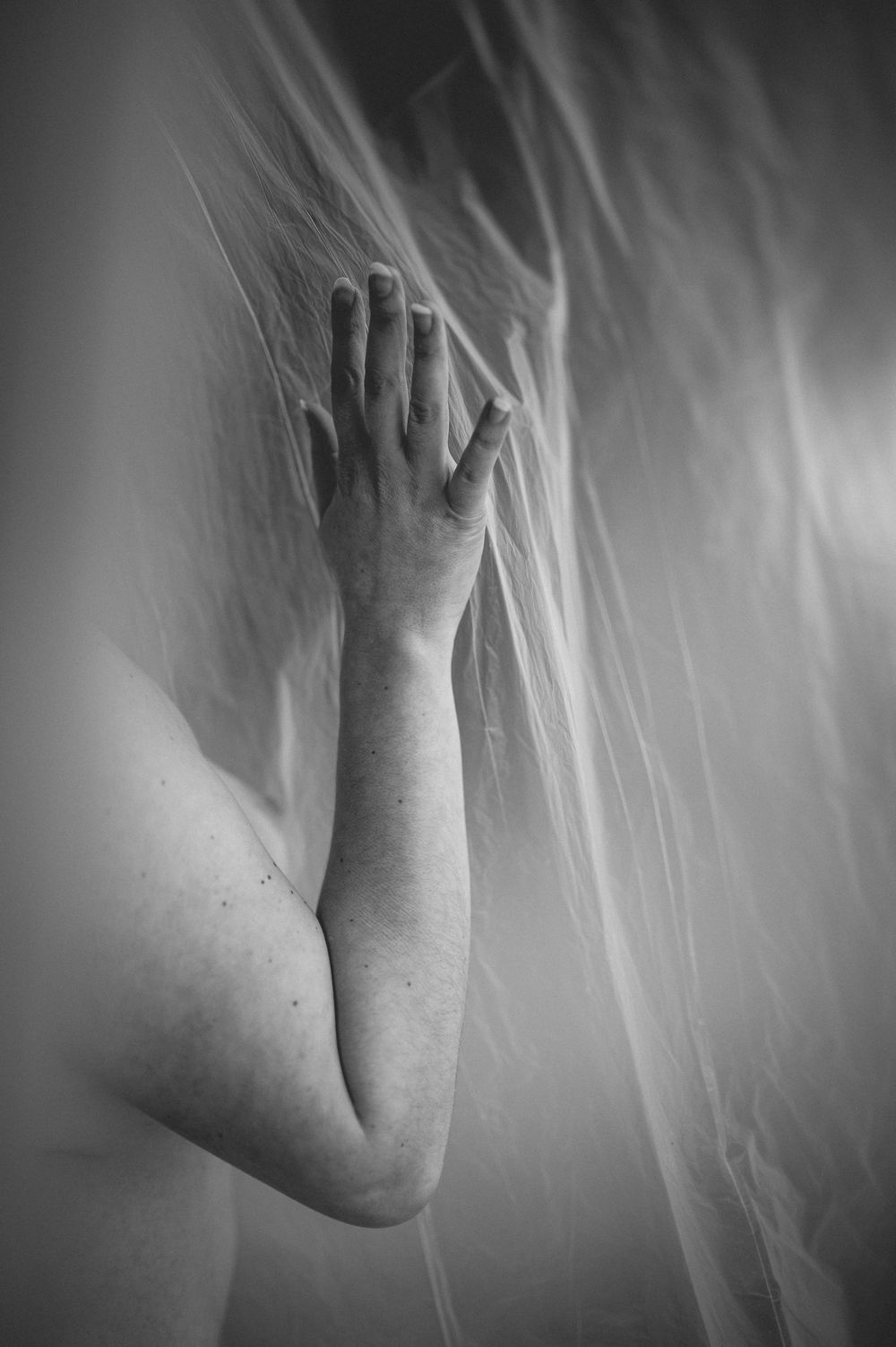 A black and white artistic photograph of an outstretched arm reaching towards wispy smoke or fabric.