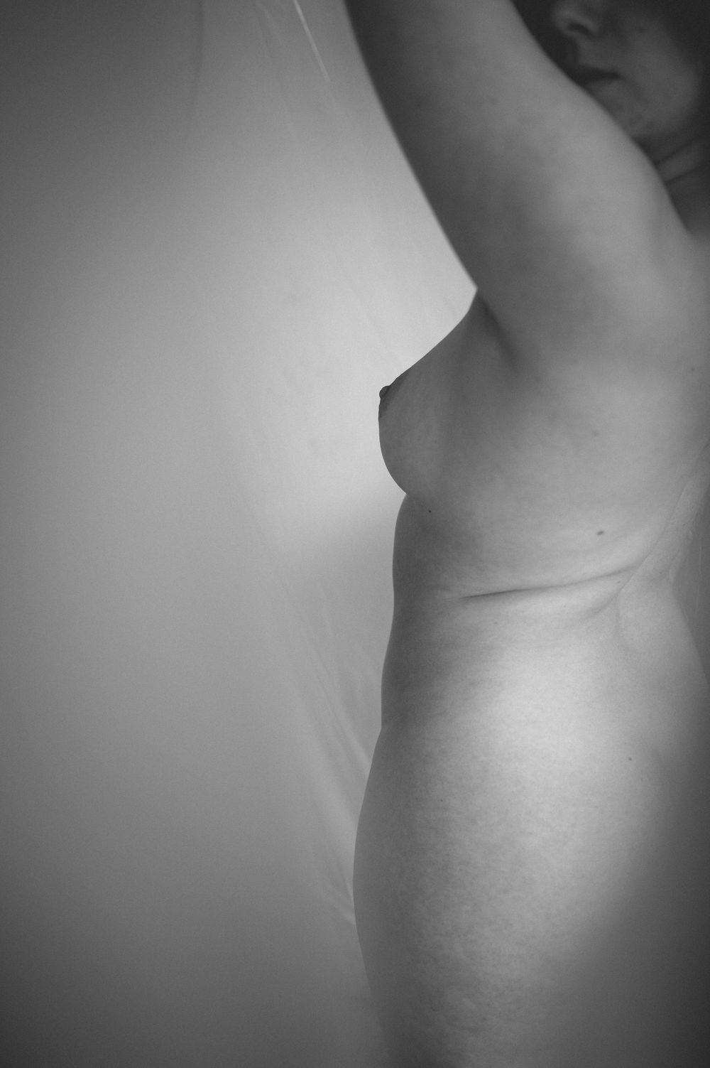 Black and white artistic nude photograph showing a side profile silhouette against a light background.