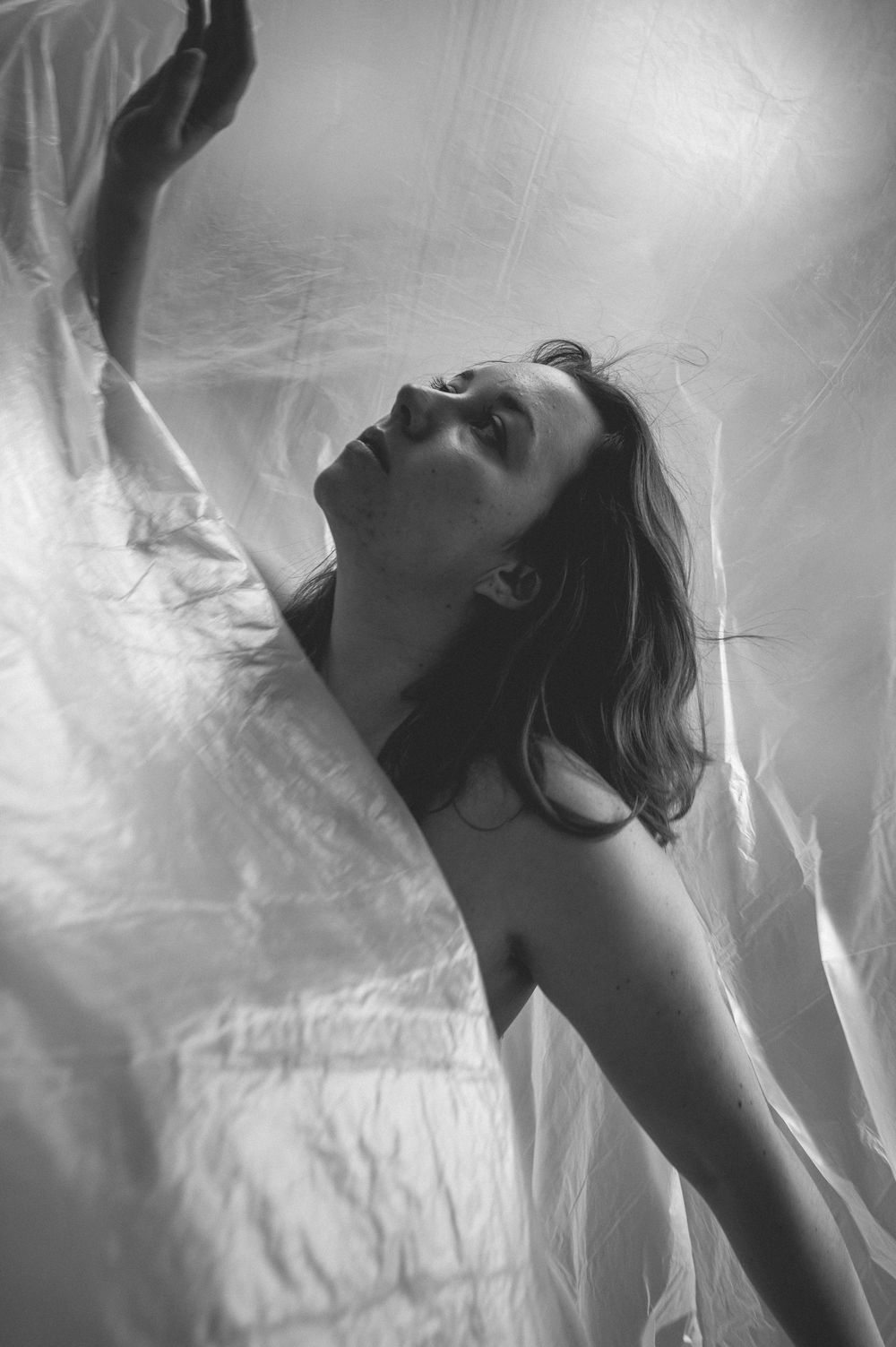 Artistic black and white portrait showing figure tilting head back with flowing fabric in dreamy ethereal lighting.