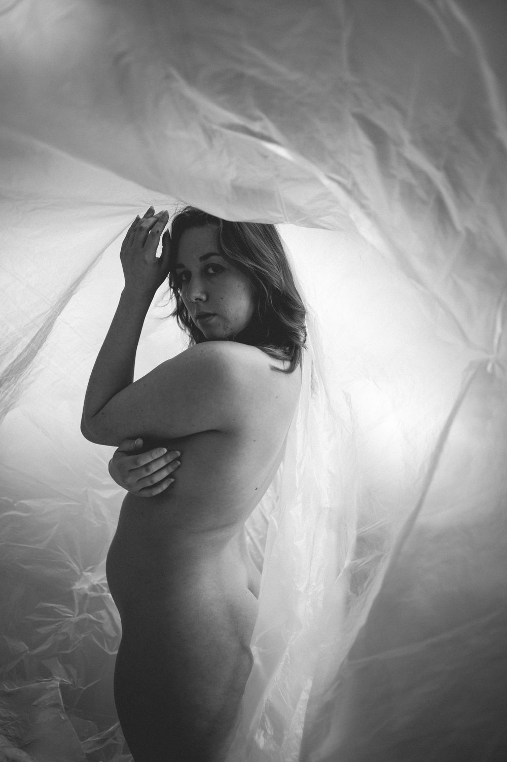 Artistic black and white boudoir photo with ethereal draped fabric creating a dreamy atmospheric effect.