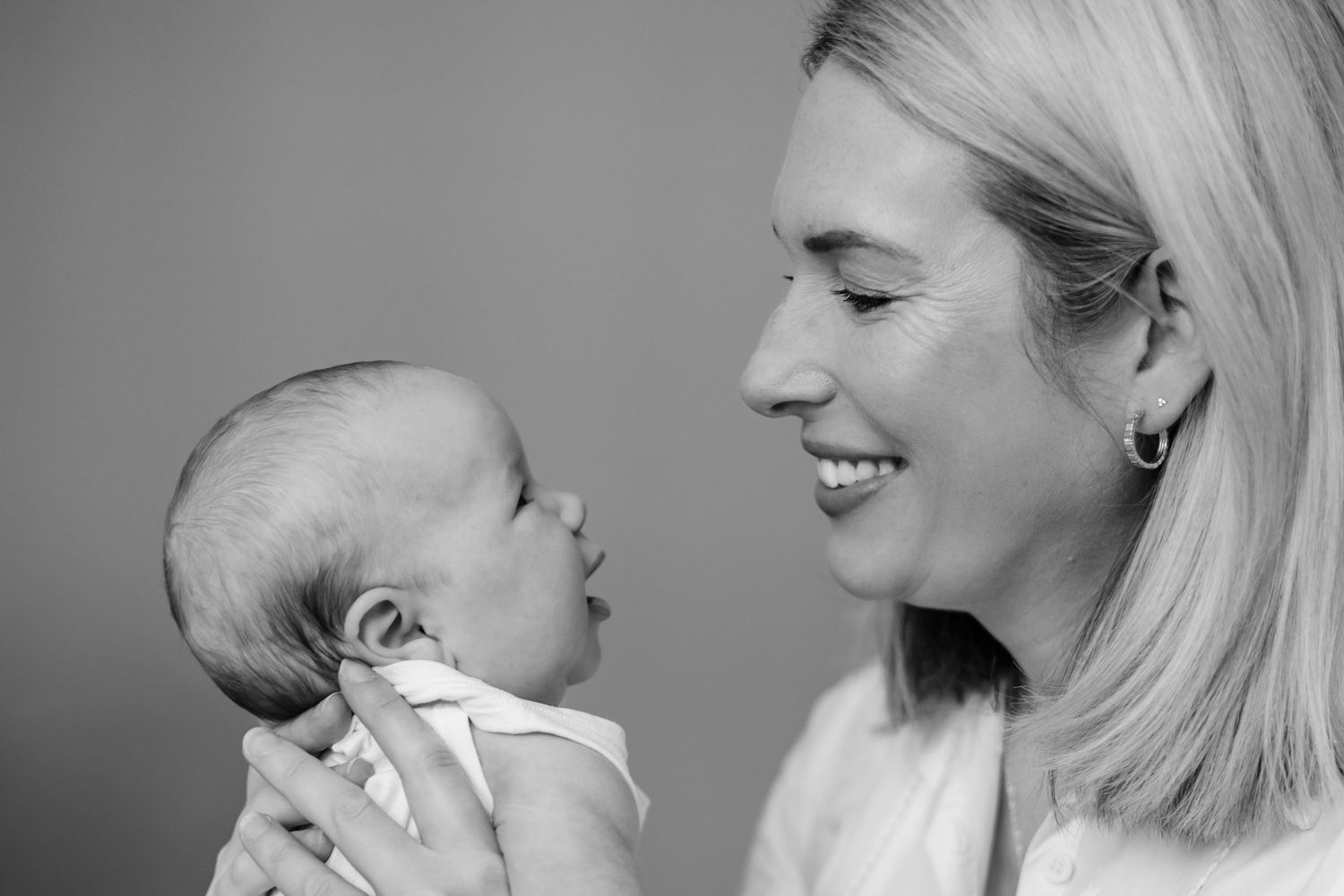 a black and white photo of a mother smiling lovingly at her baby in side-profile
