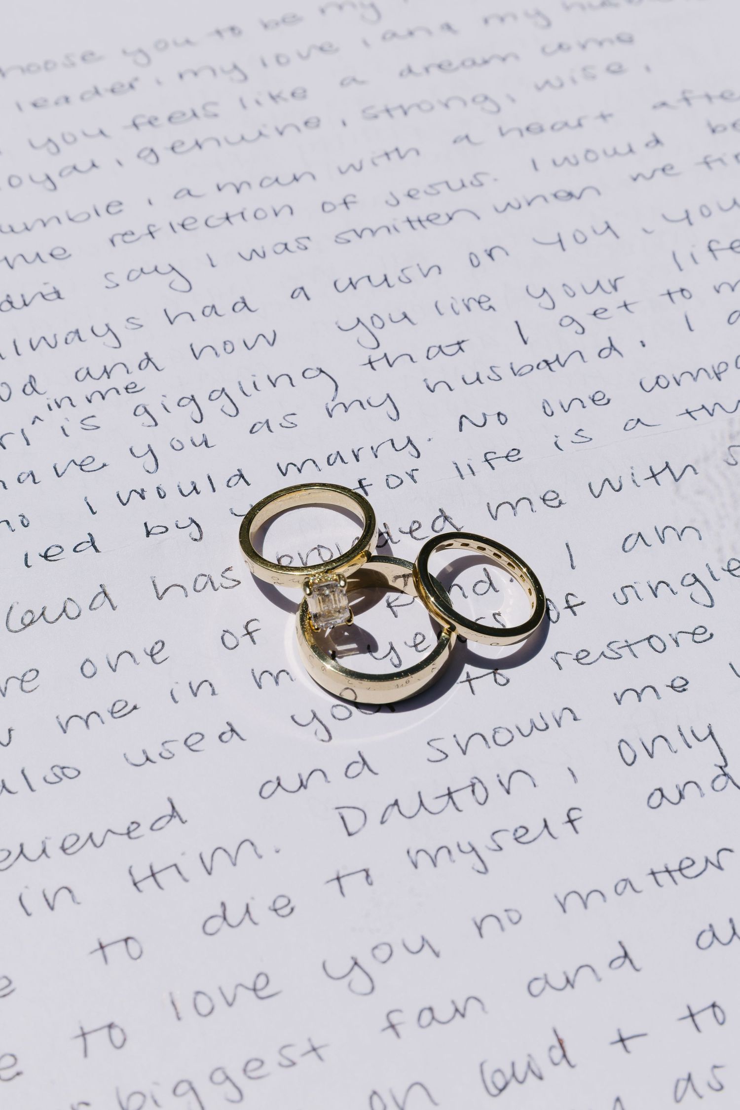 Two engagement rings rest on handwritten love letter with cursive text.