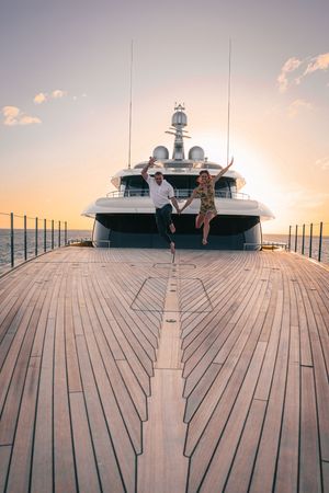 Two people pose on the deck of a luxury yacht at sunset with warm golden lighting.