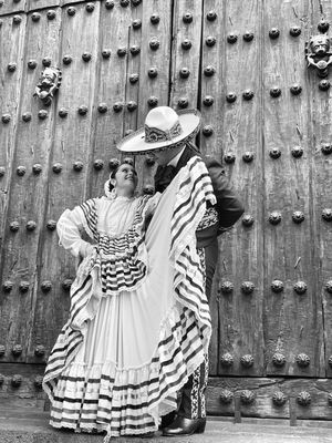 Traditional Mexican dancers in ornate black and white costumes pose against a large wooden door.