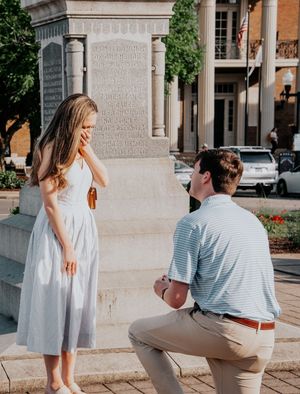 A surprise proposal moment captured on urban steps near a stone monument.