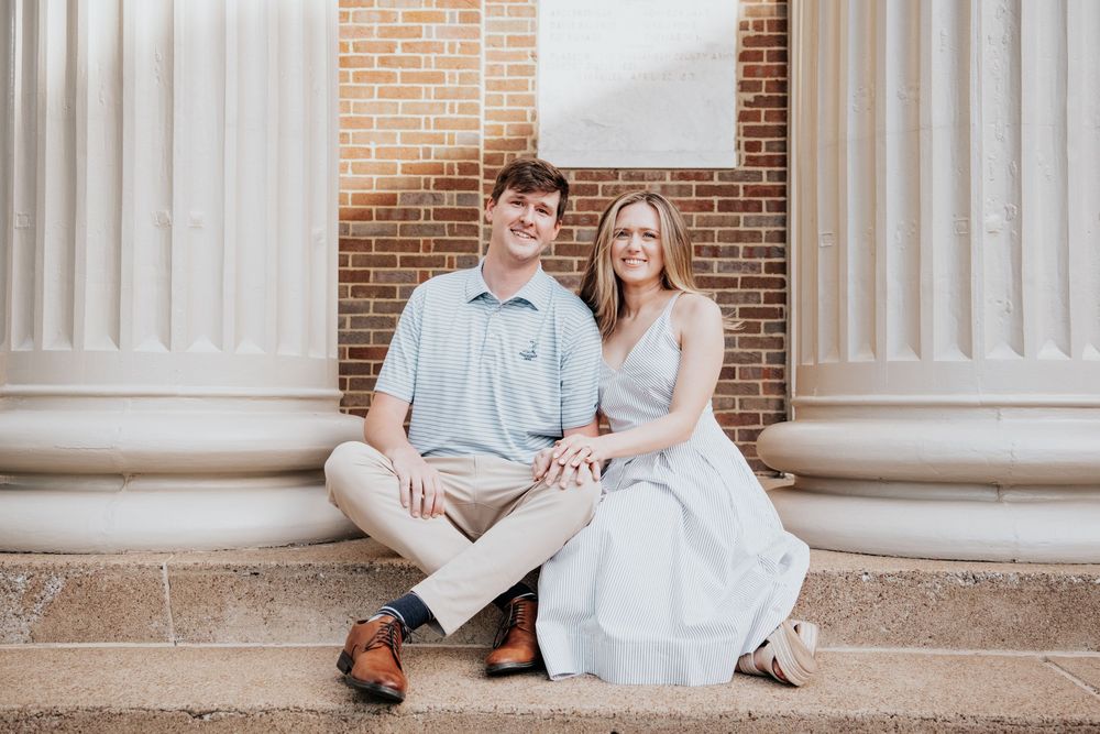 Couple poses for romantic engagement photos on columned porch in casual outfits.