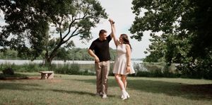 A romantic couple embraces in a scenic outdoor setting with green trees and natural lighting.