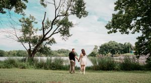 Two people walk together holding hands on a grassy hill overlooking a serene lake on a sunny summer day.