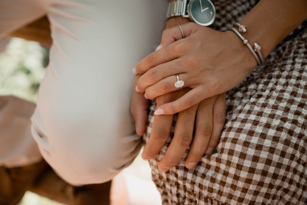 Close-up of hands showing engagement ring against checkered pattern fabric in warm lighting.