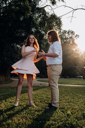 Playful couple dancing on grass during golden hour with sunlight streaming through trees.