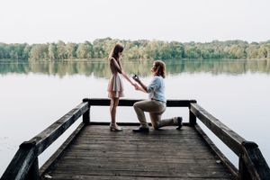 Proposal scene on a wooden dock overlooking a serene lake at sunset.