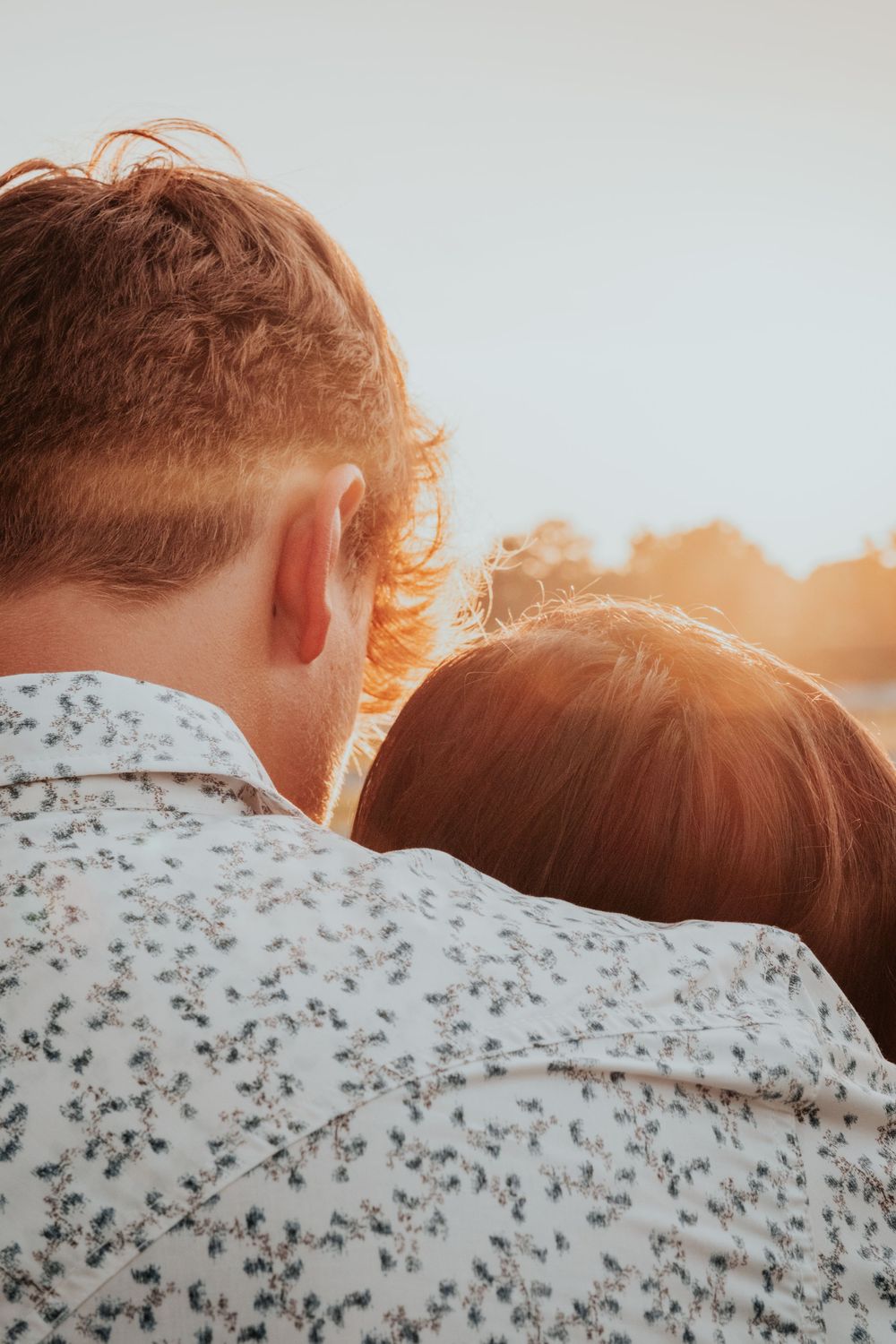 Close-up of a couple watching sunset together, silhouetted against warm golden light.
