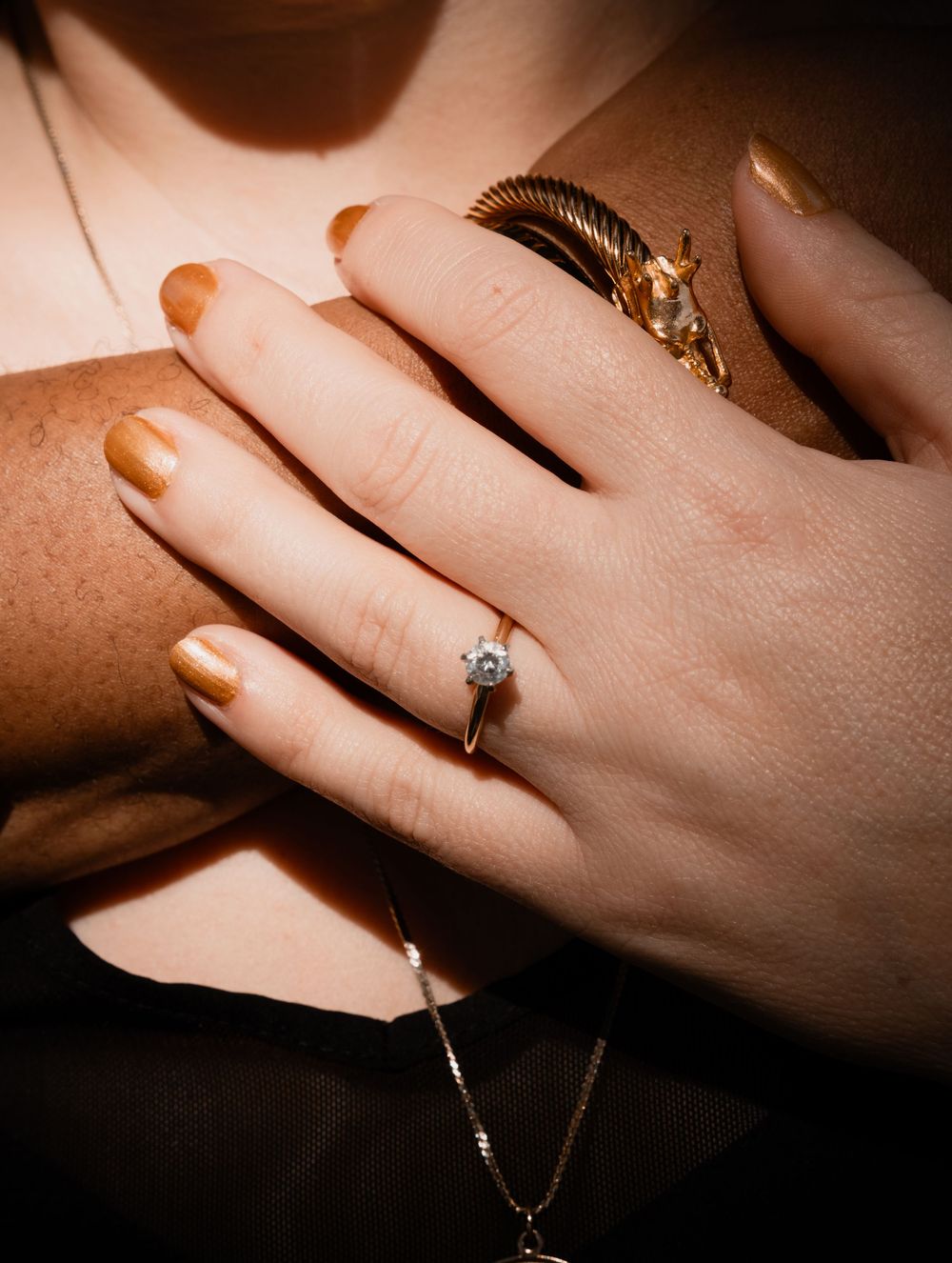 Close-up of hands wearing golden nail polish and two contrasting rings - a solitaire diamond and vintage-style gold band.