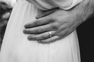 Black and white close-up of a hand with wedding ring against white fabric.