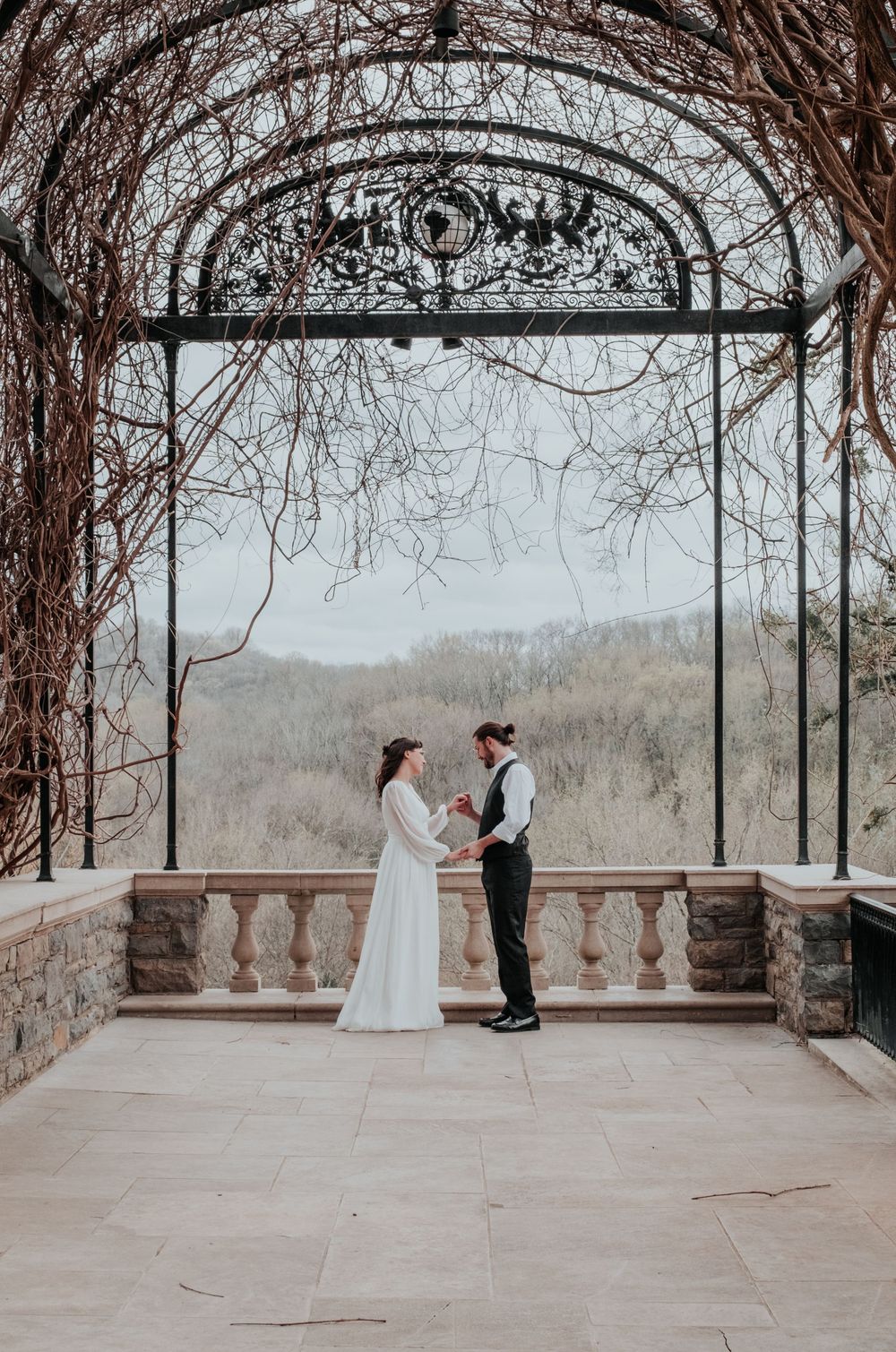 A romantic wedding photo under an ornate iron archway with mountain views in the background.