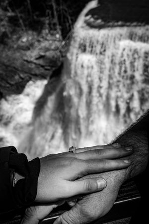 Close-up of hands near a cascading waterfall shown in black and white.